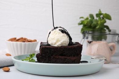 Pouring chocolate sauce onto delicious brownies with ice cream on white table, closeup