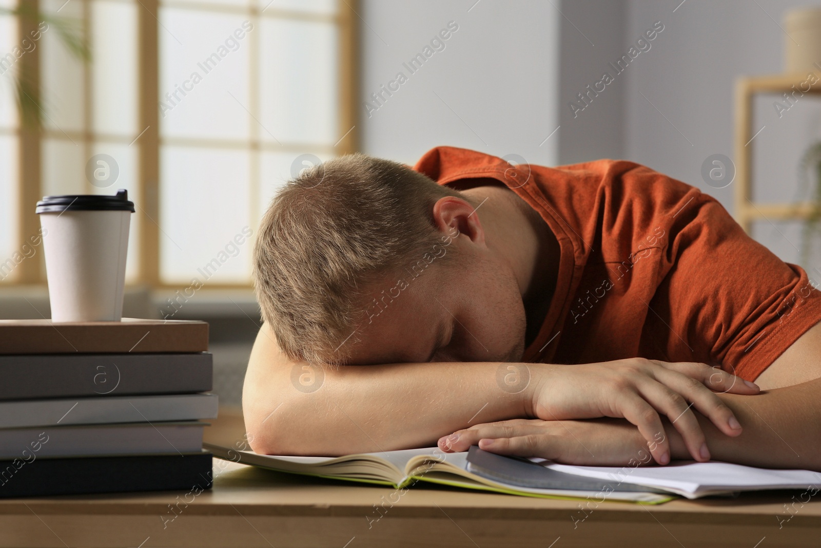 Photo of Tired man sleeping near books at wooden table indoors