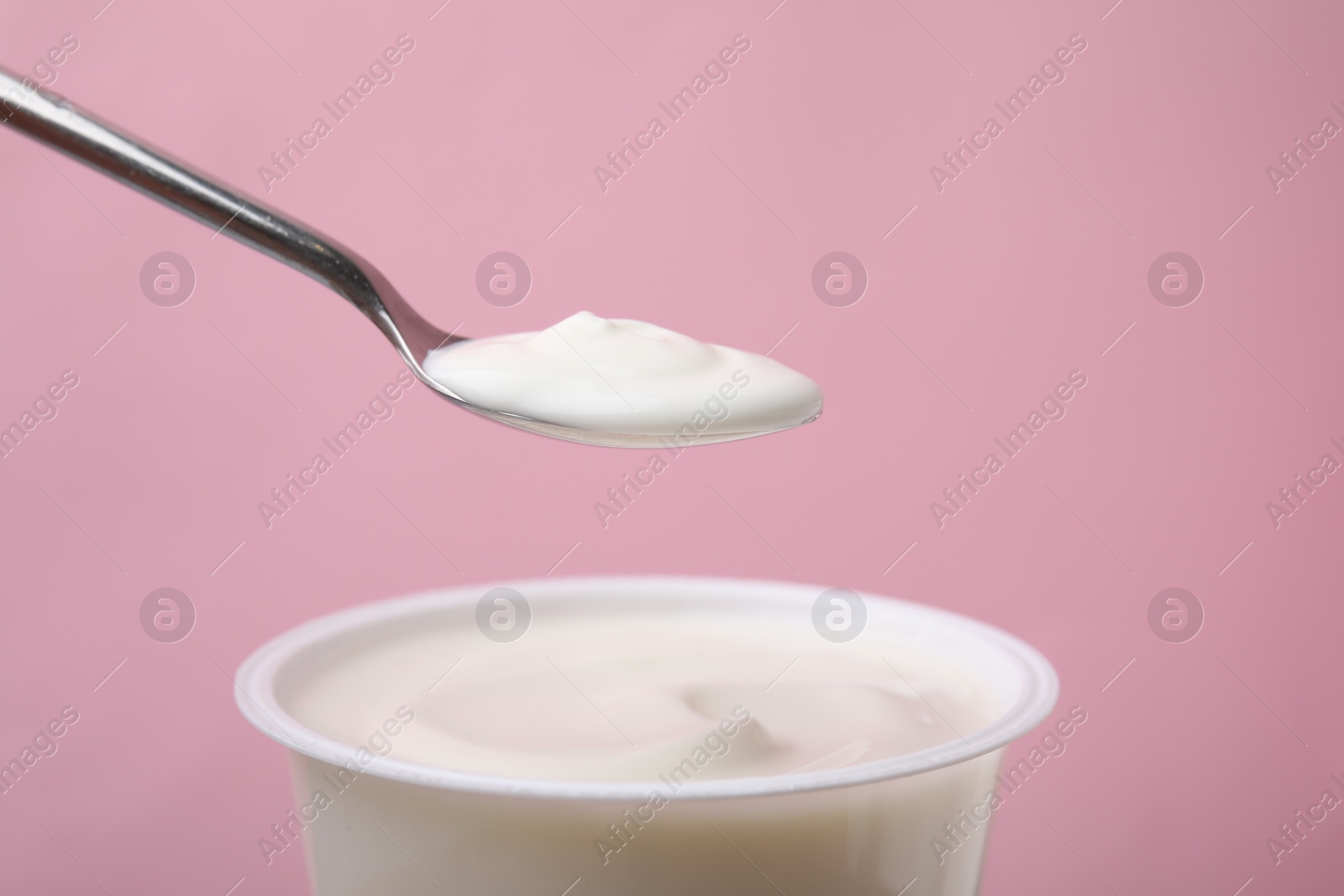 Photo of Eating delicious natural yogurt on pink background, closeup