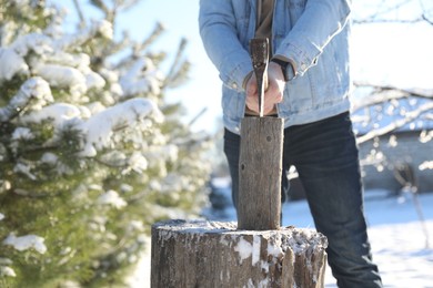 Man chopping wood with axe outdoors on winter day, closeup. Space for text