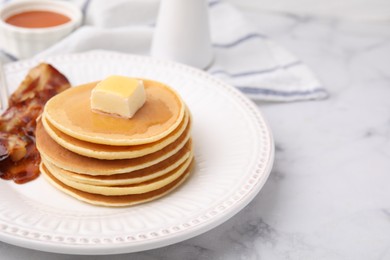 Photo of Delicious pancakes with butter, maple syrup and fried bacon on white marble table. Space for text