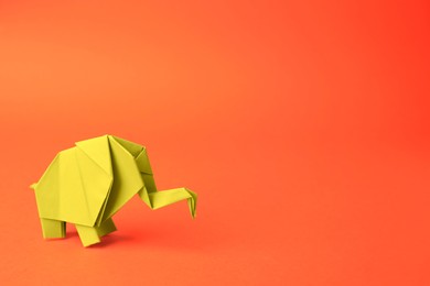 Photo of Origami art. Beautiful paper elephant on orange background, space for text