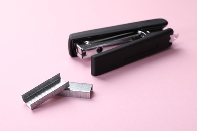 Black stapler with staples on pink background, closeup