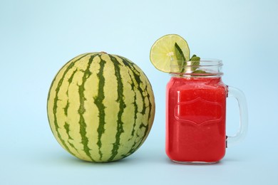 Photo of Glass of delicious drink with mint, lime and fresh watermelon on light blue background