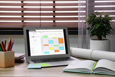 Photo of Laptop with calendar on wooden table in office