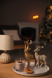 Photo of Deer figures, burning candle with lamp on wooden table and Christmas tree in living room