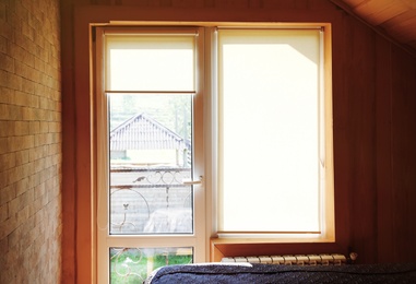 Window with roller curtains in bedroom on sunny day