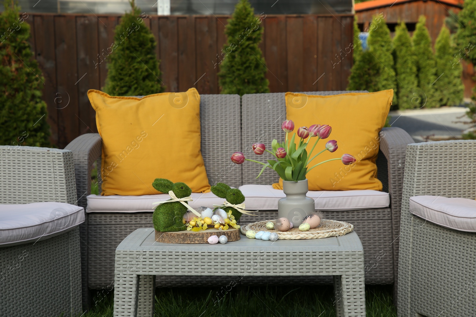 Photo of Easter decorations. Bouquet of tulips in vase, bunny figures and decorated eggs on table in backyard