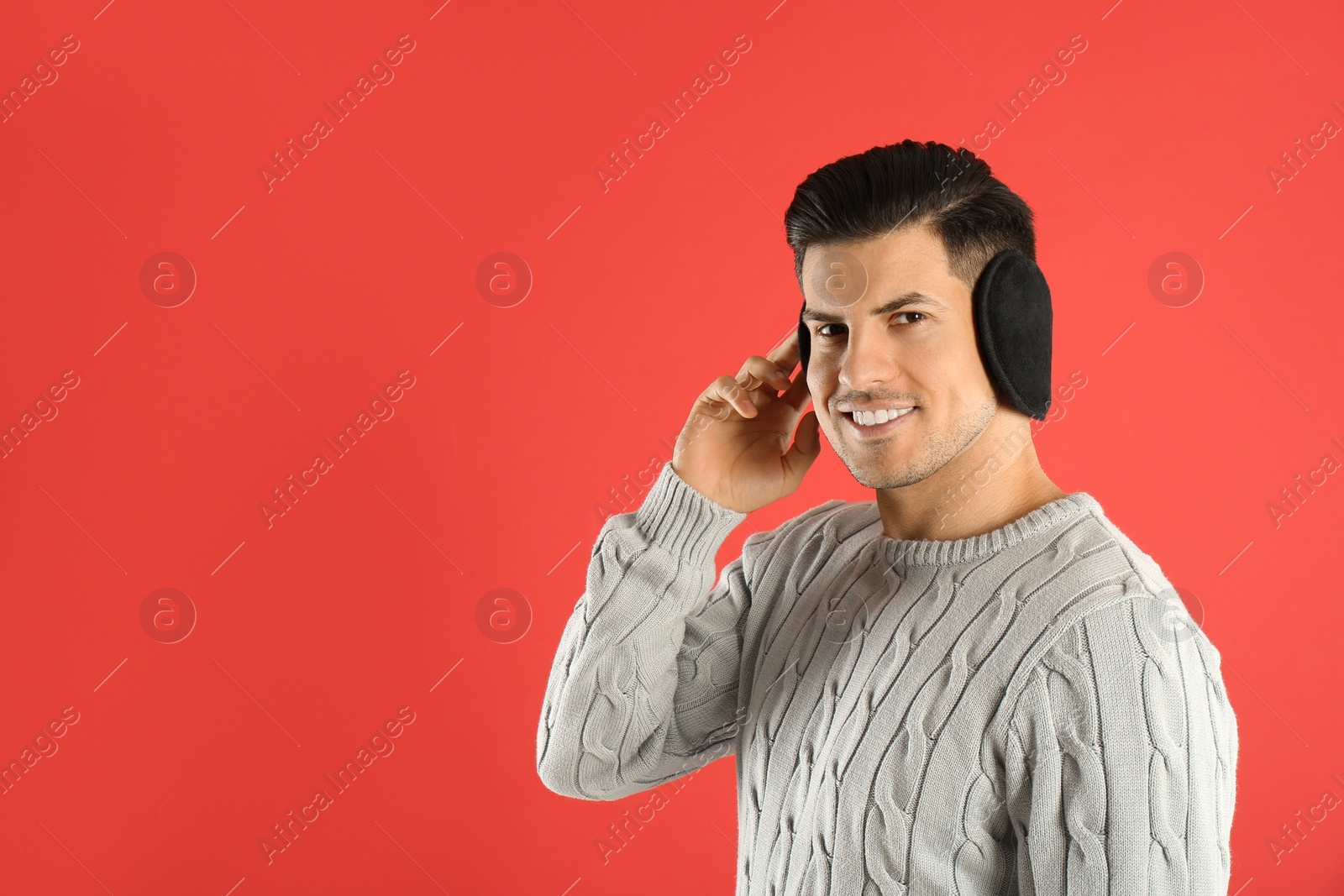 Photo of Man wearing stylish earmuffs on red background. Space for text