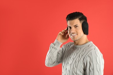 Man wearing stylish earmuffs on red background. Space for text