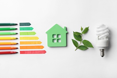 Flat lay composition with energy efficiency rating chart, fluorescent light bulb and house figure on white background