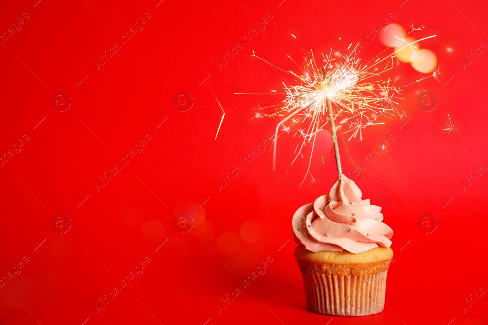 Image of Birthday cupcake with sparkler on red background. Space for text