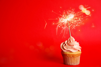 Image of Birthday cupcake with sparkler on red background. Space for text