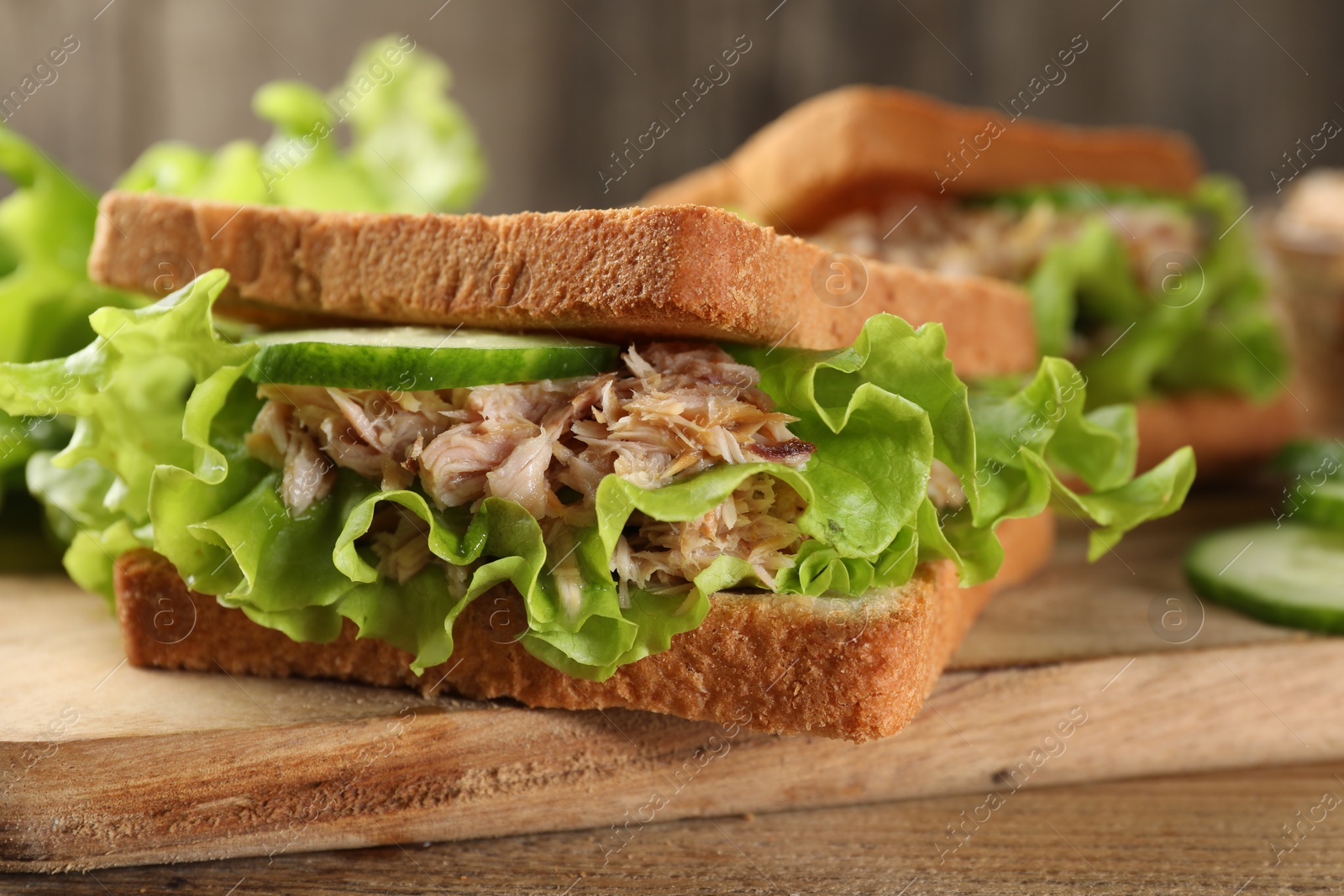 Photo of Delicious sandwiches with tuna, cucumber and lettuce leaves on wooden board, closeup