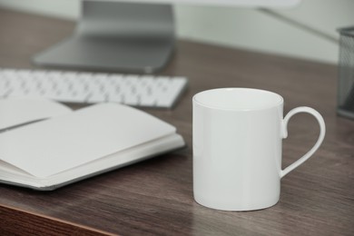 Photo of White ceramic mug on wooden table at workplace. Mockup for design