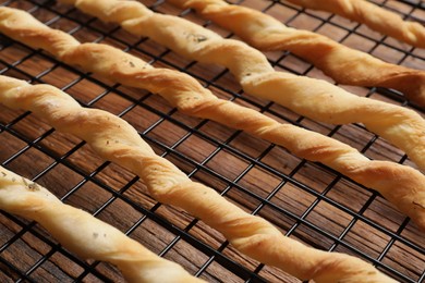 Photo of Rack with homemade breadsticks on wooden table, closeup. Cooking traditional grissini