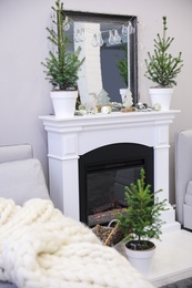 Photo of Little fir trees and Christmas decorations in room with fireplace. Stylish interior design
