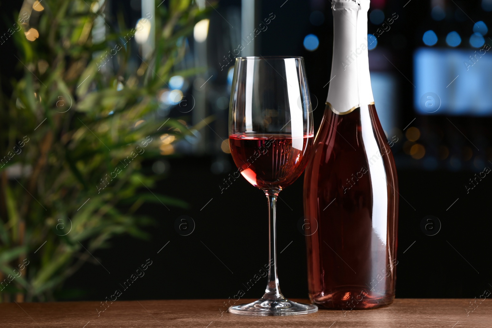 Photo of Bottle and glass of delicious rose wine on wooden table in bar. Space for text