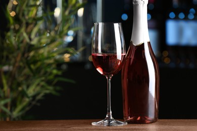 Bottle and glass of delicious rose wine on wooden table in bar. Space for text