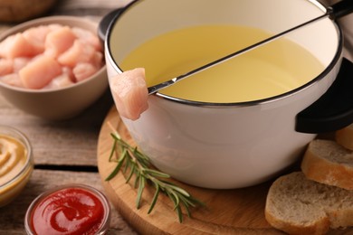 Fondue pot with oil, fork, raw meat pieces and other products on wooden table, closeup