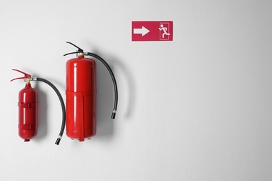 Photo of Different fire extinguishers and emergency exit sign on white wall. Space for text