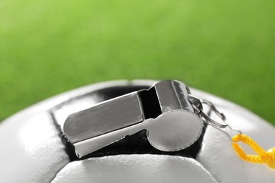Photo of Football referee equipment. Soccer ball and metal whistle on green background, closeup with space for text