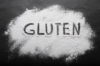Photo of Word Gluten written with flour on black table, top view