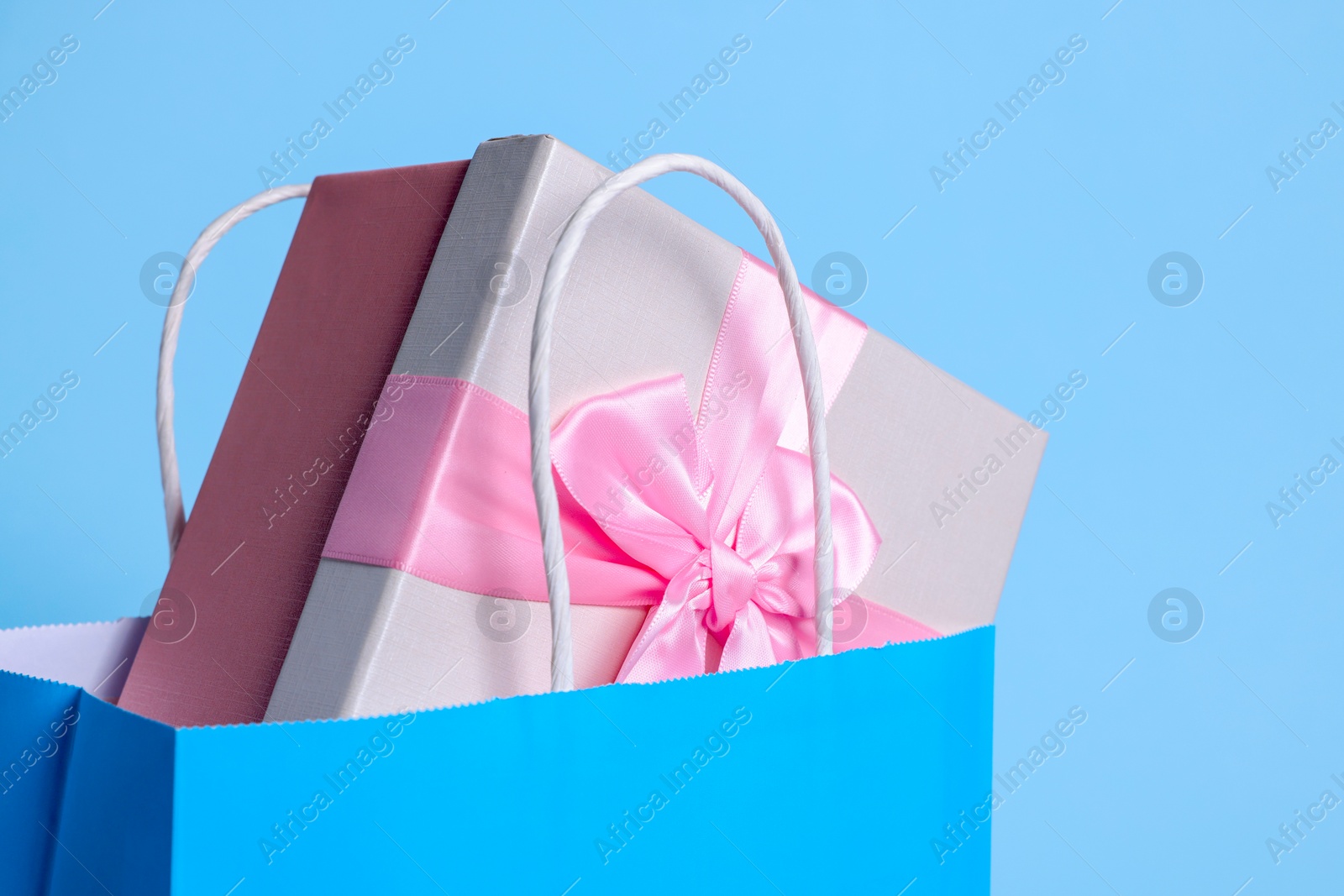 Photo of Bright paper shopping bag with gift box on light blue background, closeup