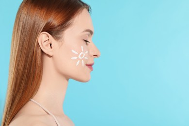 Beautiful young woman with sun protection cream on her face against light blue background, space for text