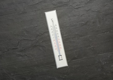 Weather thermometer on black slate background, top view