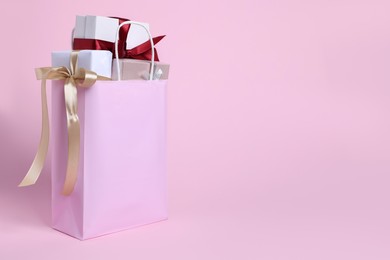 Photo of Color paper shopping bag full of gift boxes on pink background. Space for text