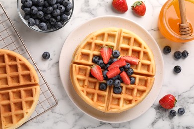 Tasty Belgian waffles with fresh berries and honey on white marble table, flat lay
