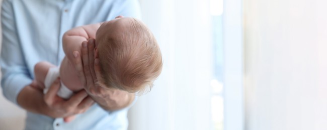 Father holding his newborn baby at home, closeup view with space for text. Banner design