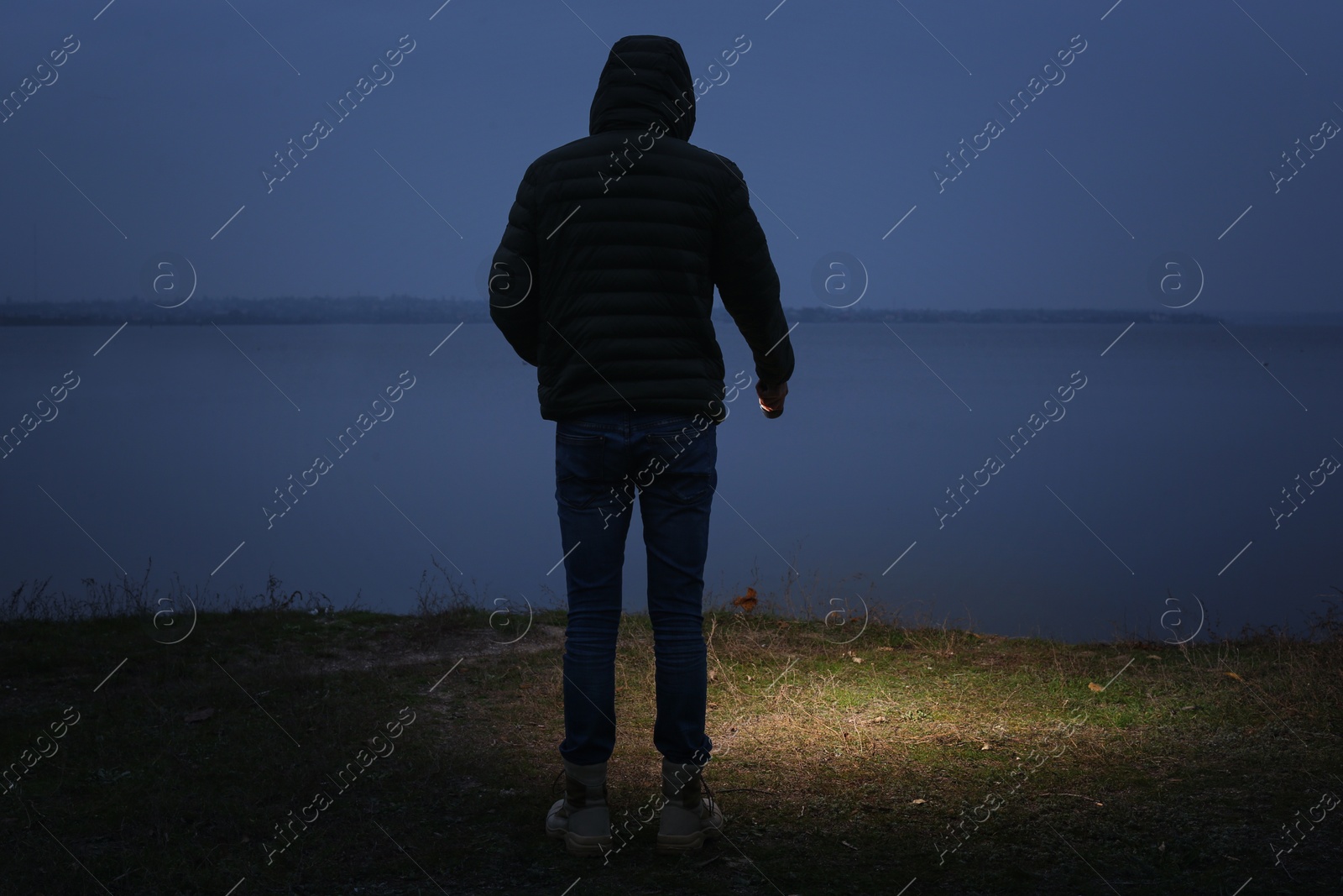 Photo of Man with flashlight walking near river in evening