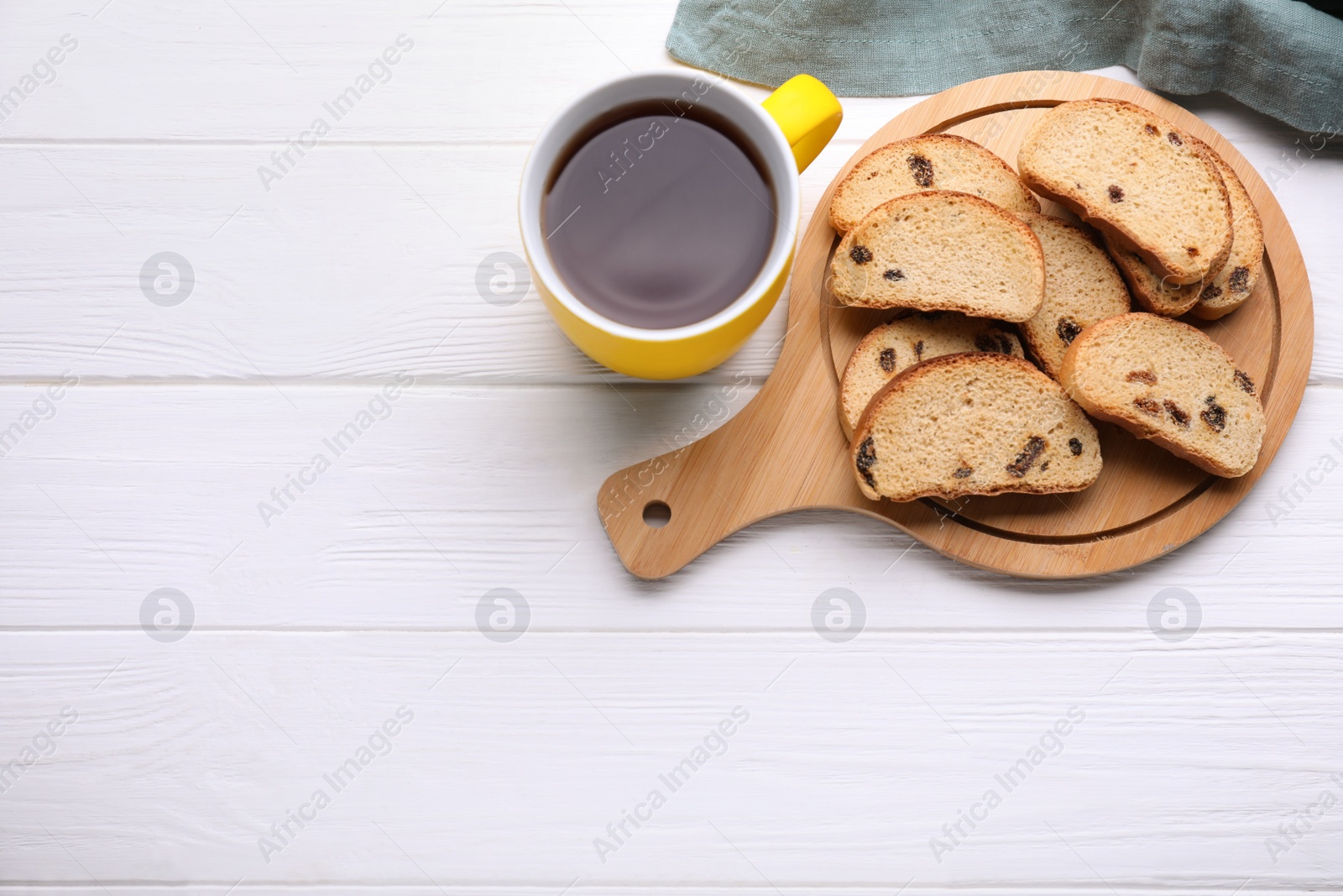 Photo of Sweet hard chuck crackers with raisins and cup of tea on white wooden table, flat lay. Space for text