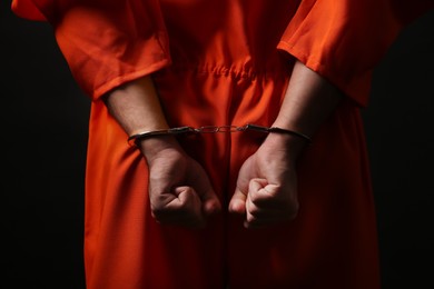 Photo of Prisoner in jumpsuit with handcuffs on black background, closeup