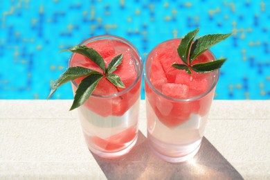 Photo of Refreshing watermelon drink in glasses near swimming pool outdoors