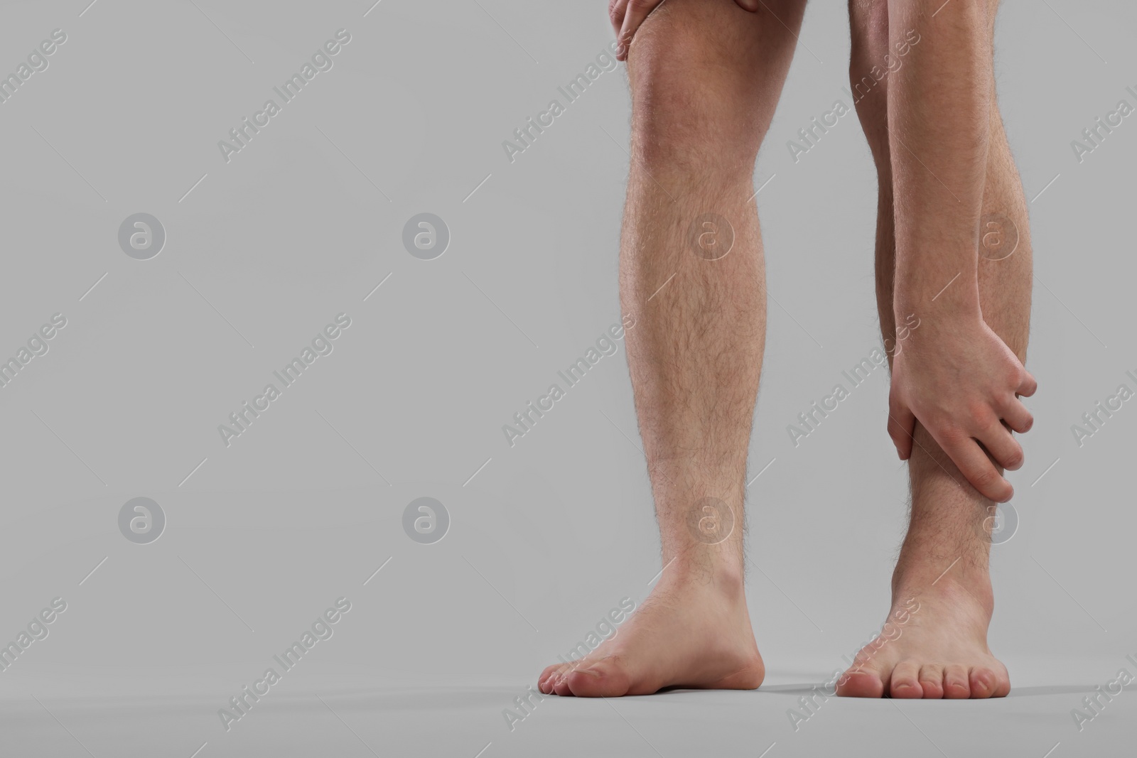 Photo of Man suffering from leg pain on grey background, closeup. Space for text