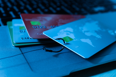 Fishing hook with credit cards and laptop on table, closeup. Cyber crime