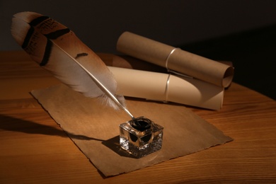 Feather pen, inkwell and blank parchment on table in darkness