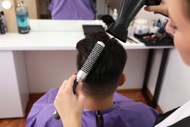 Photo of Professional hairdresser drying client's hair in salon, closeup