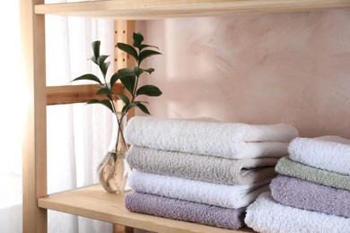 Photo of Stacked soft towels and green leaves on wooden shelf indoors