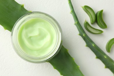 Photo of Jar with cream and cut aloe leaves on white table, flat lay