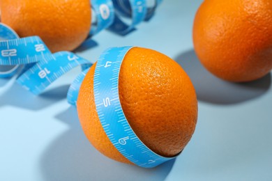 Photo of Cellulite problem. Orange with measuring tape on light blue background, closeup