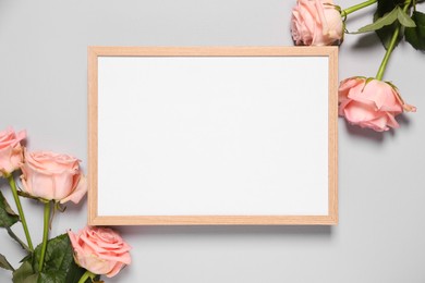 Photo of Empty photo frame and beautiful flowers on light background, flat lay. Space for design