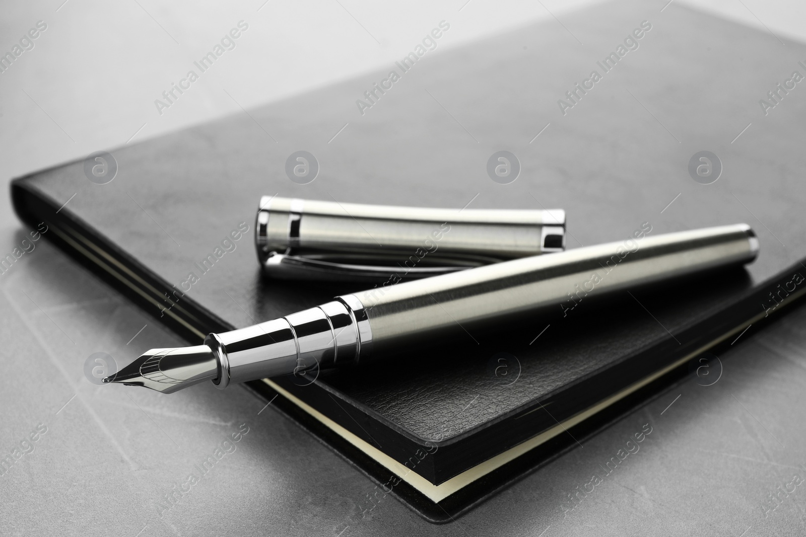 Photo of Stylish fountain pen, cap and leather notebook on light grey textured table, closeup