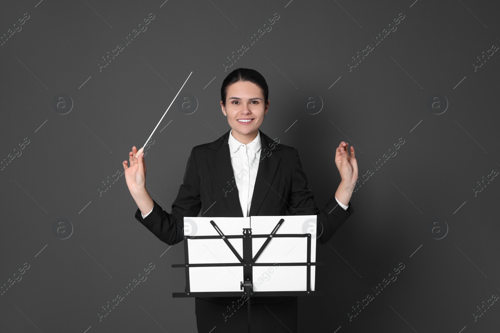 Photo of Happy professional conductor with baton and note stand on grey background