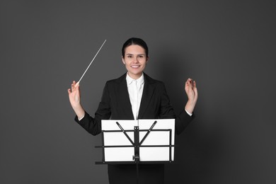 Happy professional conductor with baton and note stand on grey background
