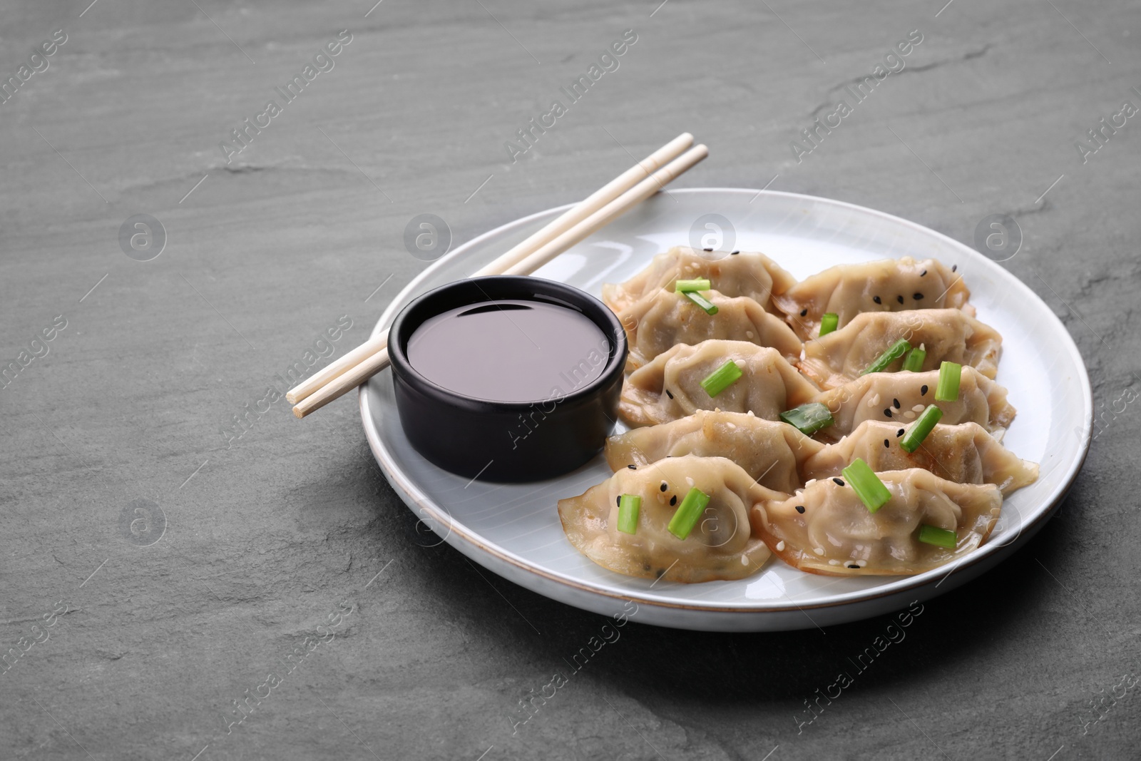 Photo of Delicious gyoza (asian dumplings) with green onions, soy sauce and chopsticks on gray table, space for text