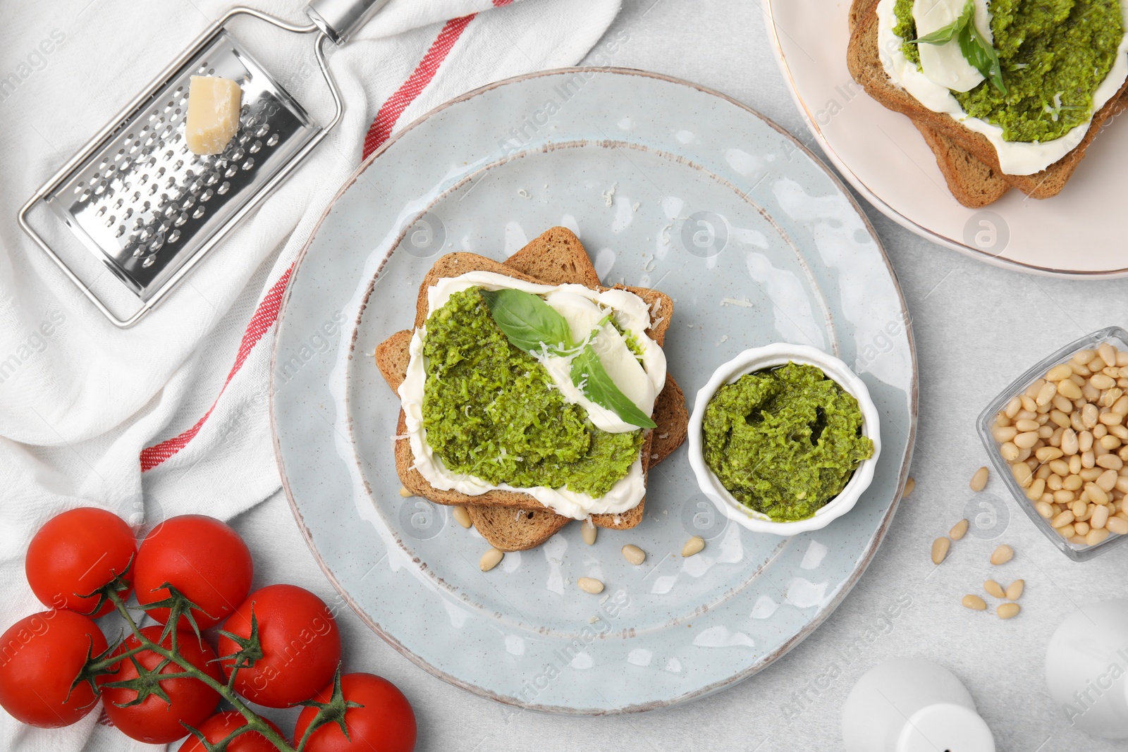 Photo of Tasty bruschettas with cream cheese, pesto sauce and fresh basil on light gray table, flat lay